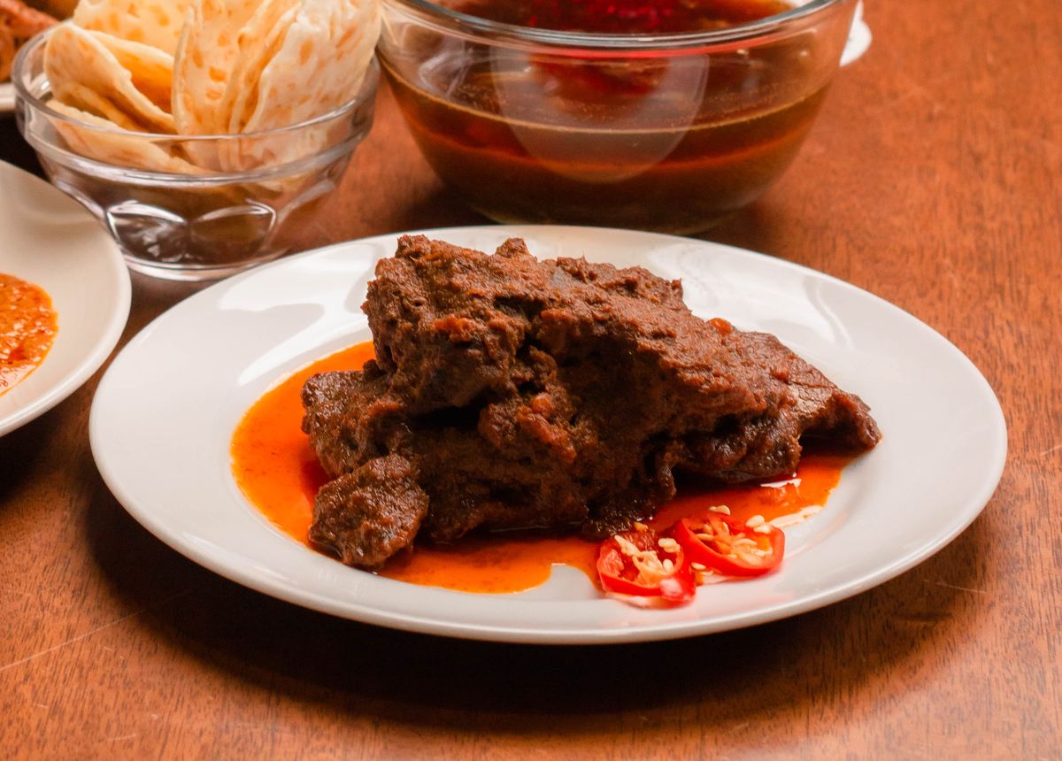 A plate of dark, slow-cooked beef rendang with sliced red chilli and crispy sides